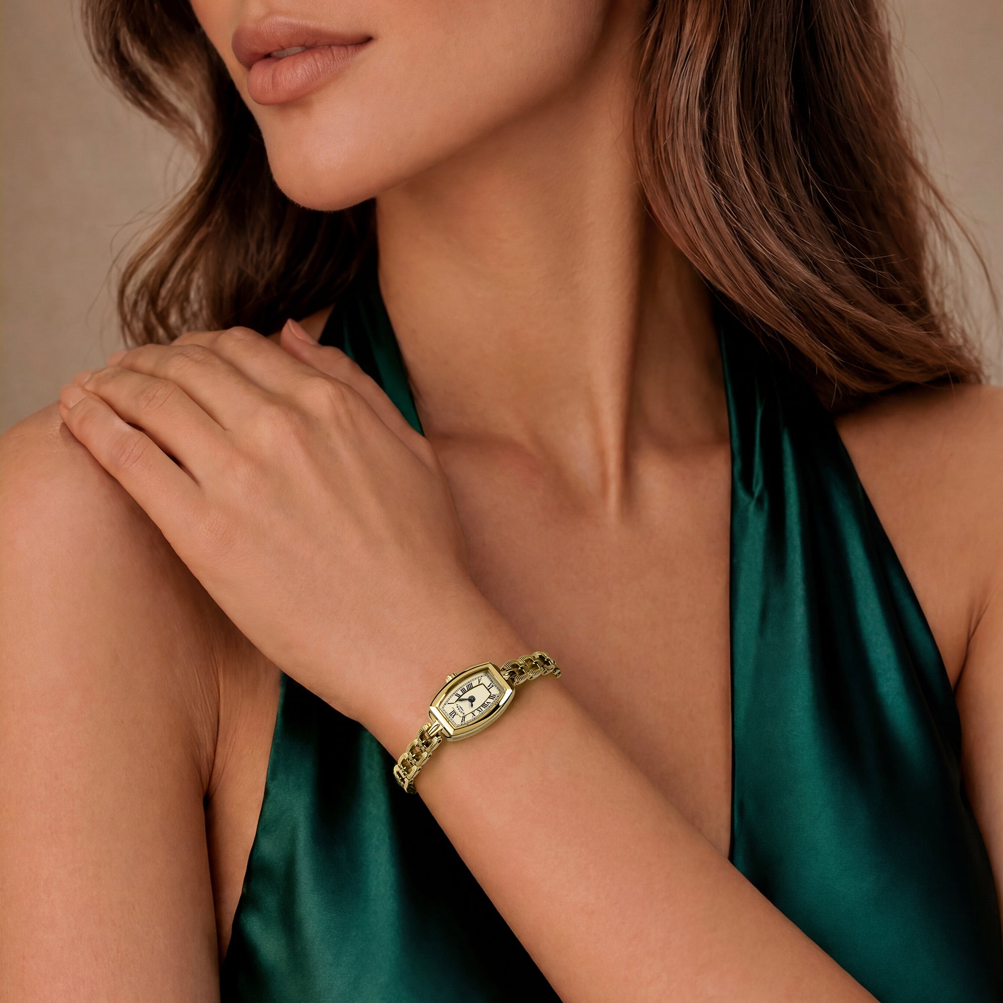 Woman wearing a gold Rotary bracelet with a green satin top, on a neutral background
