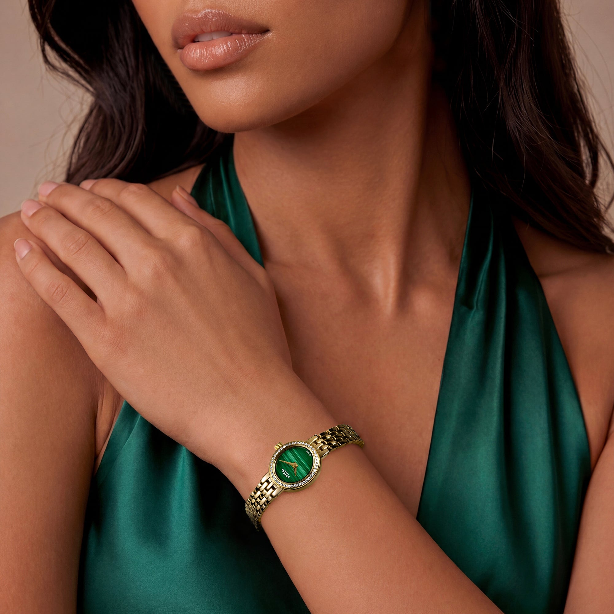 Woman wearing a gold Rotary Cocktail bracelet watch with a green stone dial on a beige background