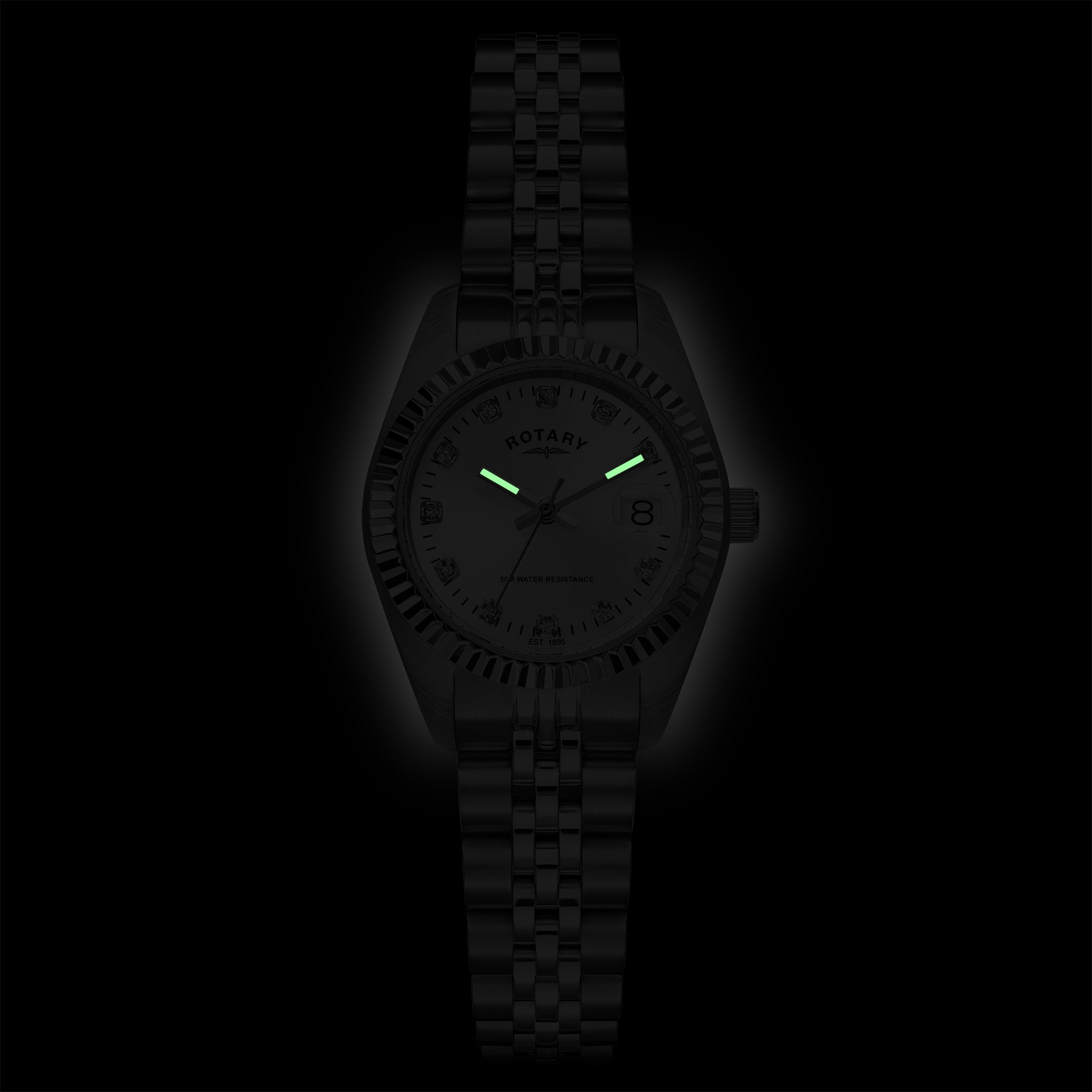 A dark, low-light studio shot of a Rotary wristwatch with a black metal case and link bracelet, featuring glowing green hands and a black dial with white markings on a black background.