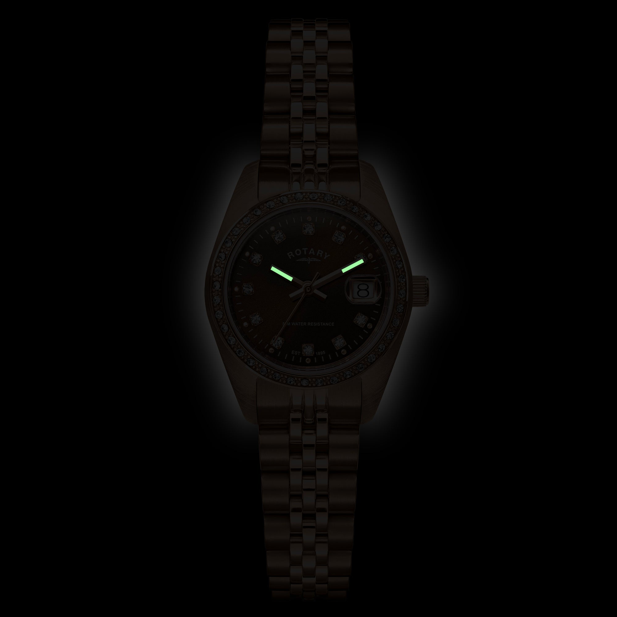 A dark brown Rotary Dress Date watch with a matching link bracelet, shown in a low-light setting to highlight its green luminescent hands and dial details.