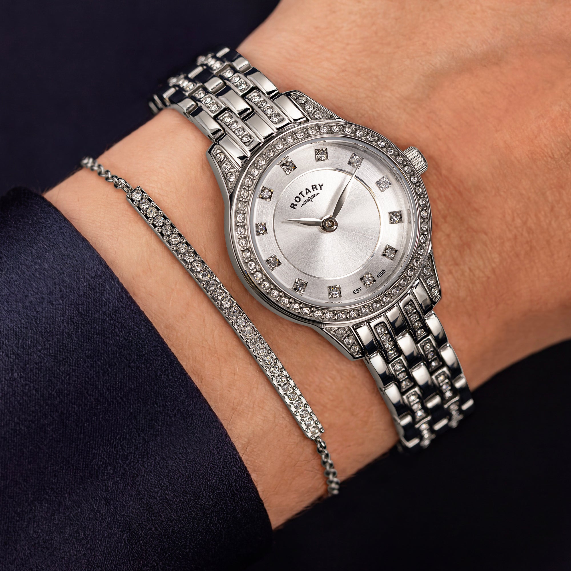 A silver-tone metal bracelet Rotary watch with a gem-set bezel and silver dial, worn on a wrist alongside a matching gem-embellished bracelet.