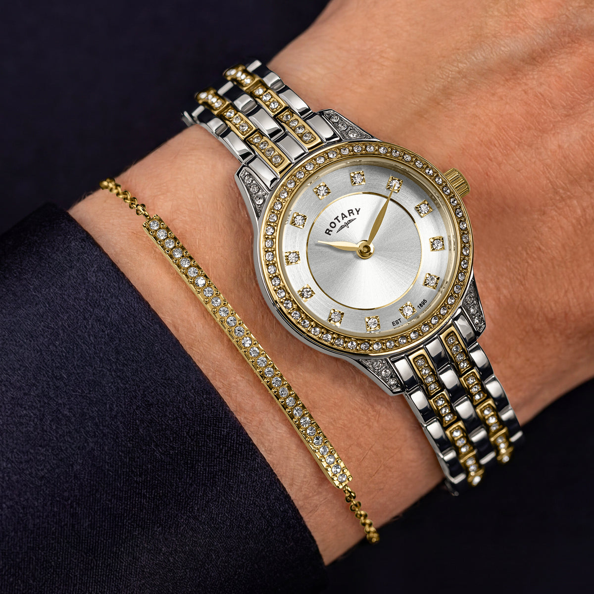A two-tone silver and gold watch with a gem-set bezel and white dial, shown on a person's wrist alongside a matching gold tennis bracelet.