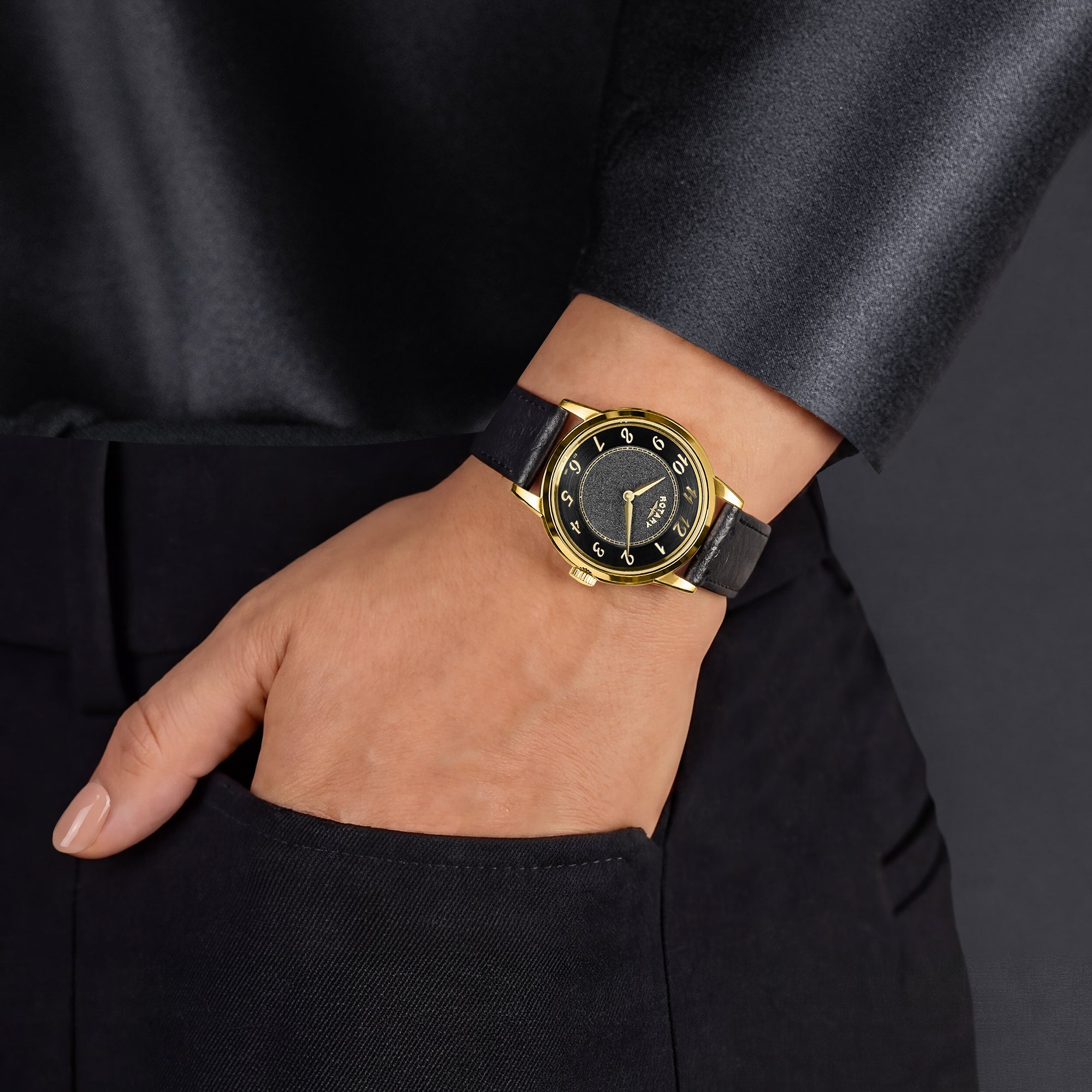 A woman wearing a blackleather strap gold Rotary watch with gold accents on a dark background