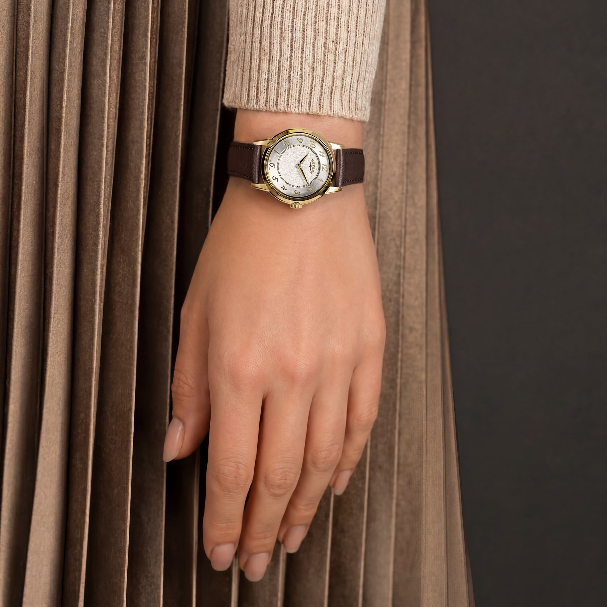 A woman wearing a gold Rotary ladies watch with a brown strap.
