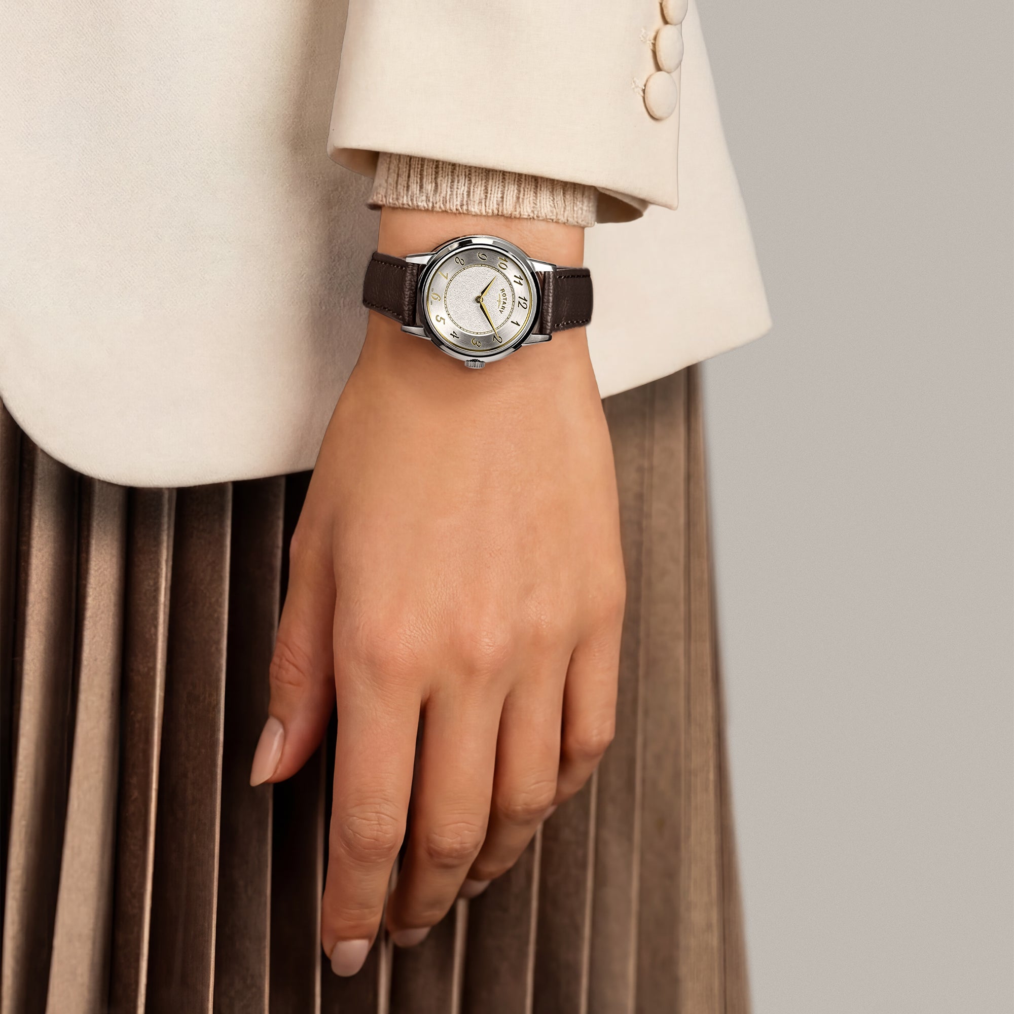 A woman wearing a silver Rotary watch with a brown strap against a neutral background