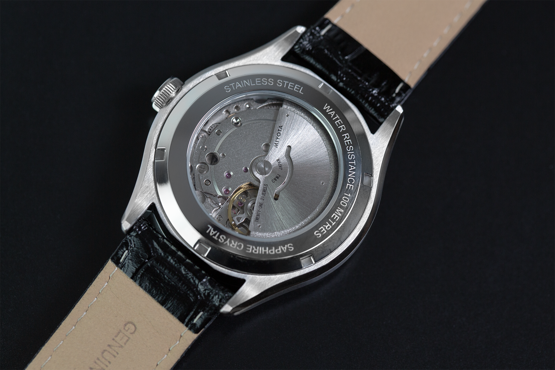 Close-up of a Seamatic 100 watch with a black leather strap and visible mechanical components on a dark background.