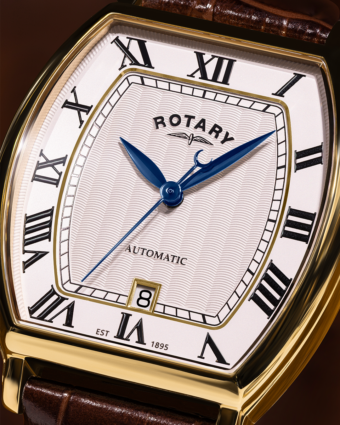 Rotary 1895 Tonneau automatic  watch with gold case, brown leather strap, and white face with black Roman numerals.