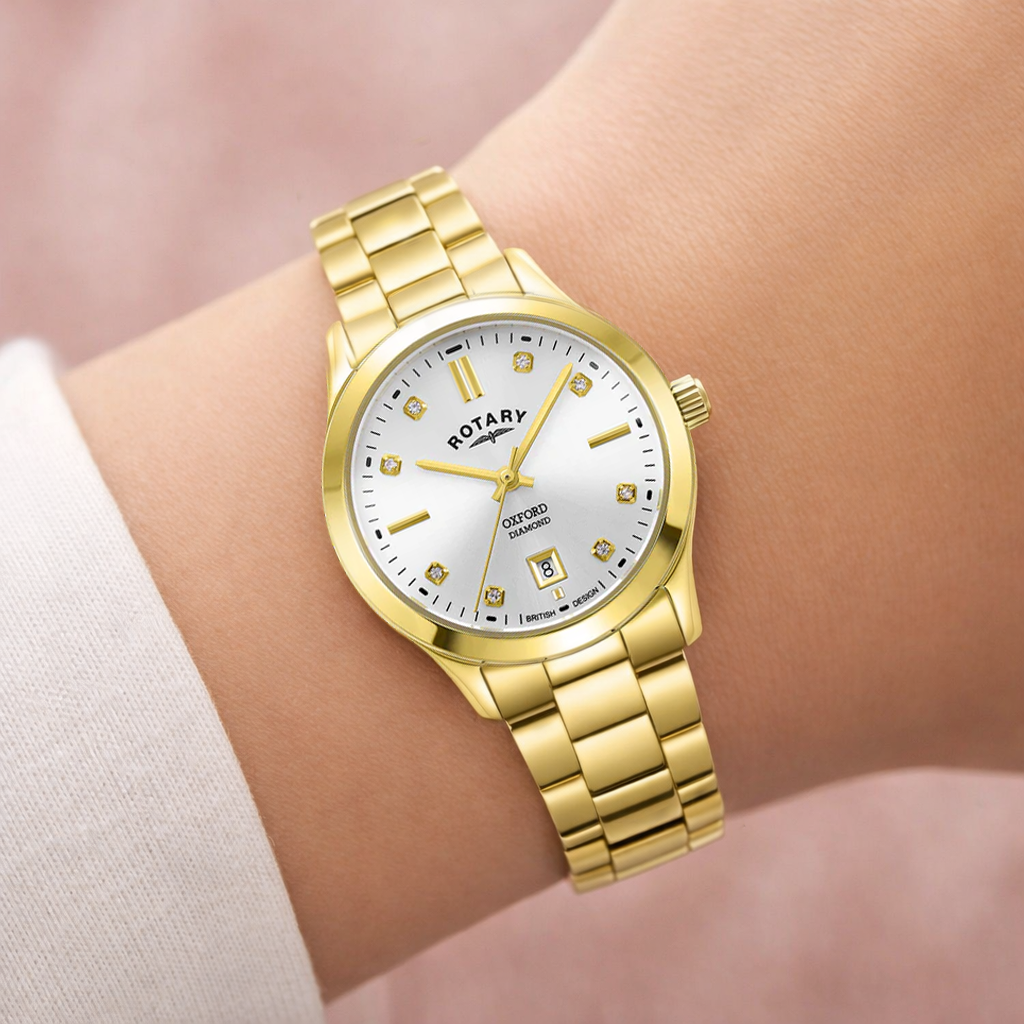 Gold Rotary Oxford Diamond wristwatch with white dial on a wrist against a soft pink background