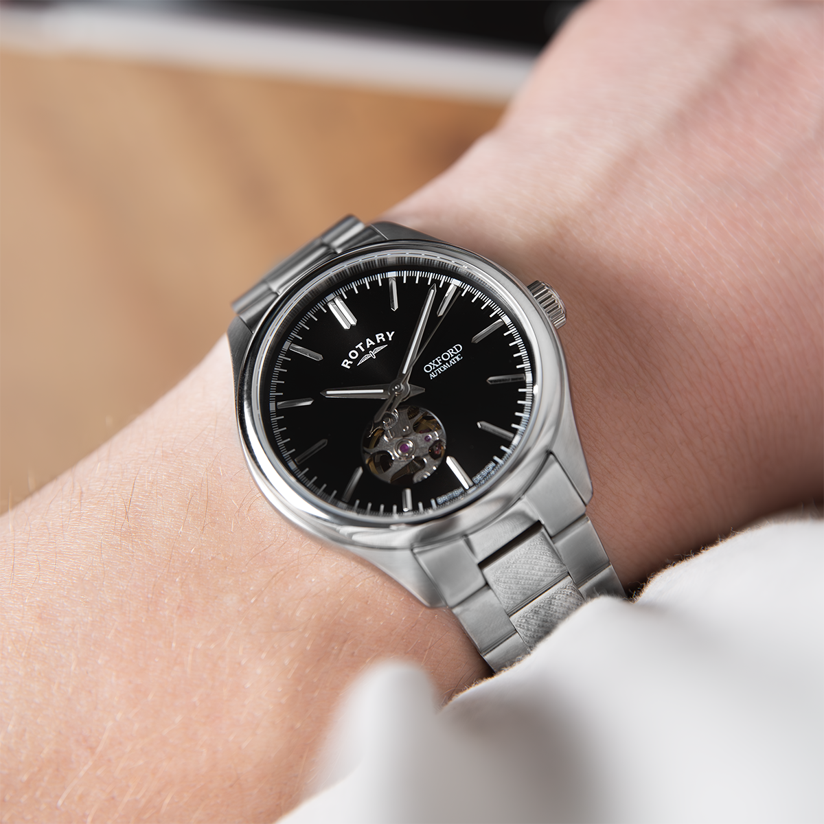 Silver rotary watch with black dial on a wrist against a neutral background