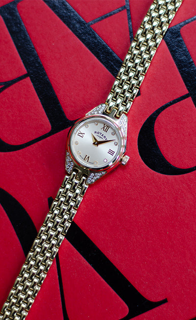 a rotary ladies watch in gold with gem and diamond setting on a red book